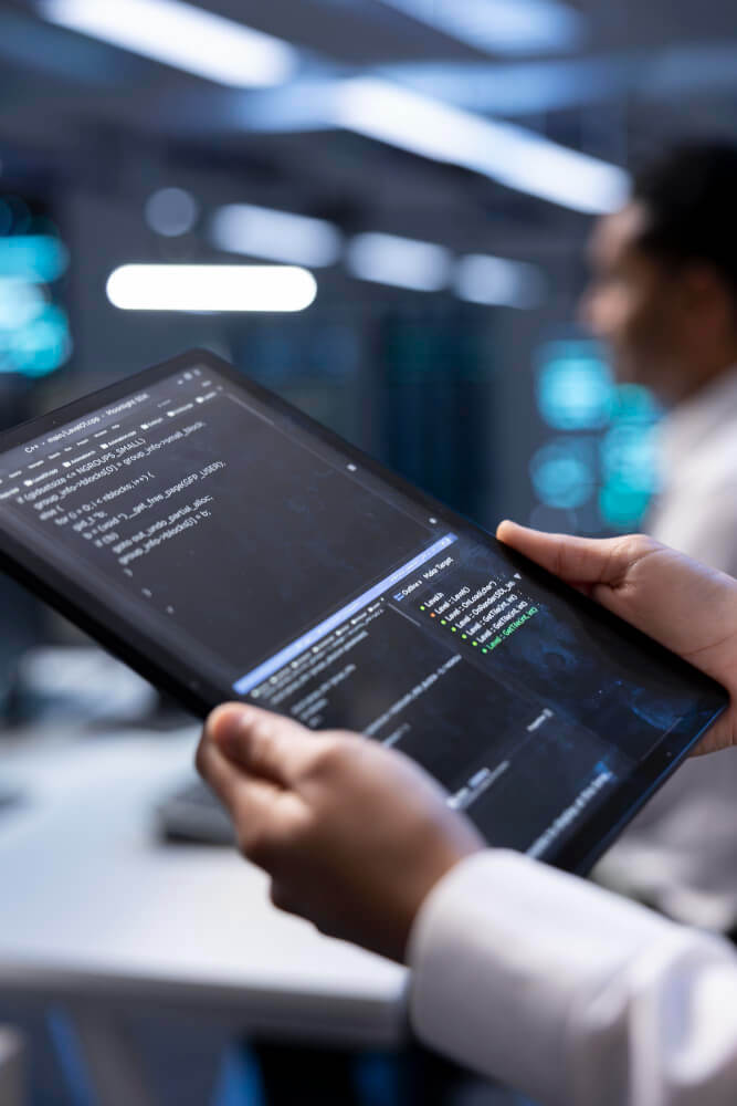 Close-up of a person holding a tablet displaying programming code and data in a modern tech environment, symbolizing software development and data analysis.